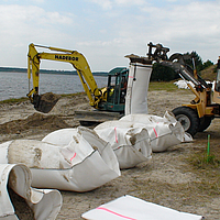 Filling with locally available sand of the SoilTain Bags with the help of an excavator while wheel loader holds up the prefabricated sand bag