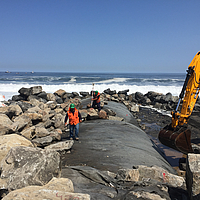 Fully installed hose is covered with armor stones with the help of an excavator