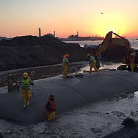 Installation and filling of a hose with the help of an excavator and construction workers standing on the almost completely filled hose