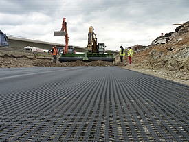 Soil is tipped onto half-laid Fortrac MDT Geogrid rolls, for reinforcement in alkali-resistant applications and soils with extreme pH values