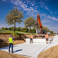 Excavator with laying traverse rolls out Stabilenka geogrid on construction site